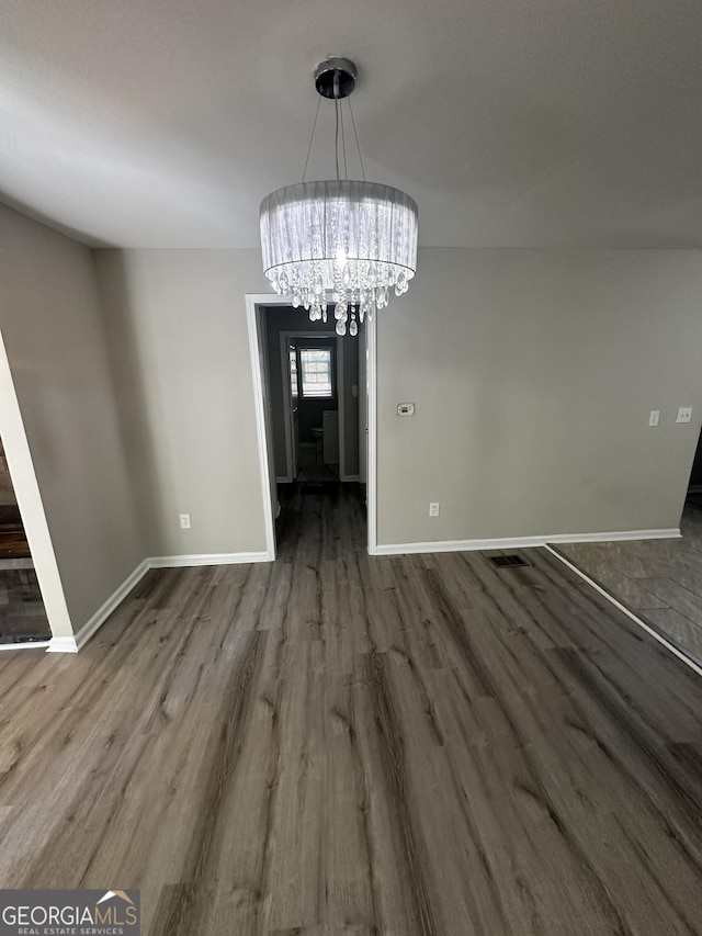 unfurnished dining area featuring a chandelier, baseboards, and wood finished floors