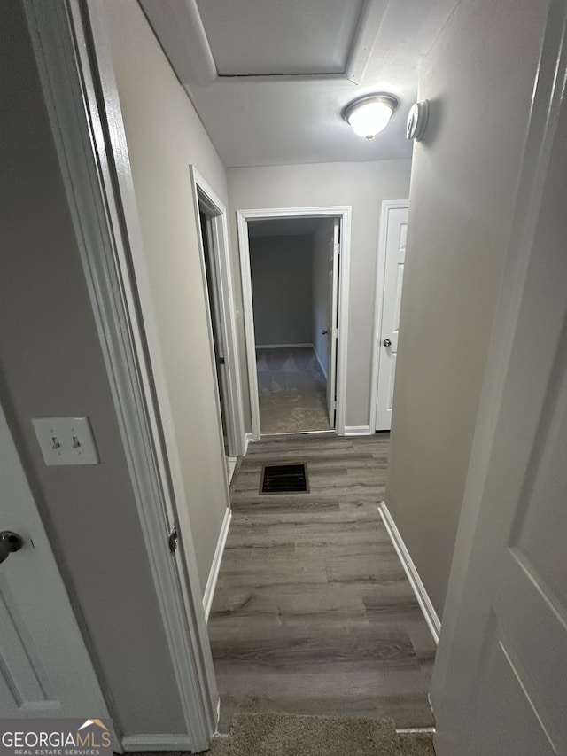 hall featuring attic access, visible vents, baseboards, and wood finished floors