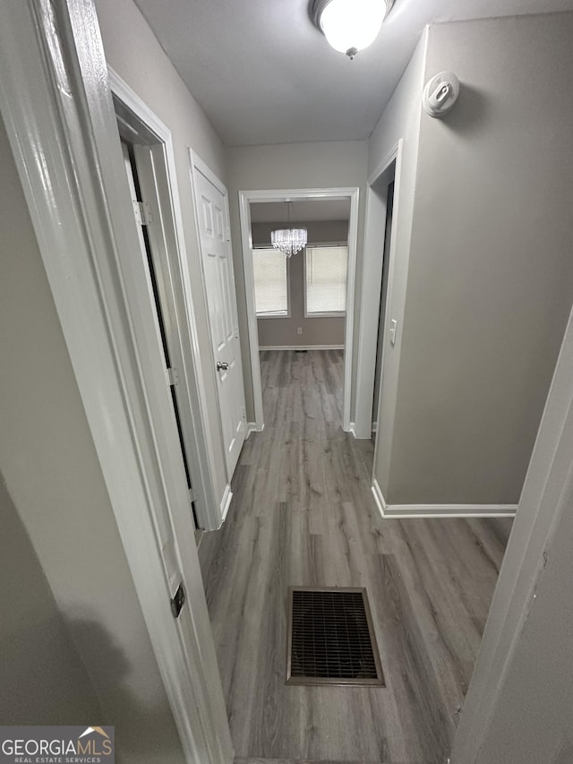 corridor with a notable chandelier, wood finished floors, visible vents, and baseboards