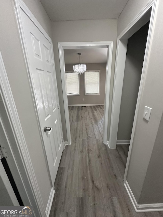 corridor featuring a notable chandelier, baseboards, and wood finished floors