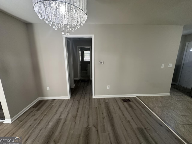 unfurnished dining area featuring a chandelier, baseboards, and dark wood-style floors