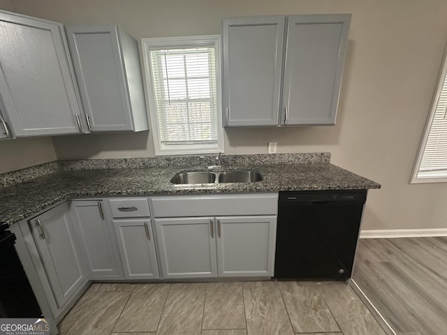 kitchen featuring black dishwasher, range, light wood-style flooring, dark stone countertops, and a sink