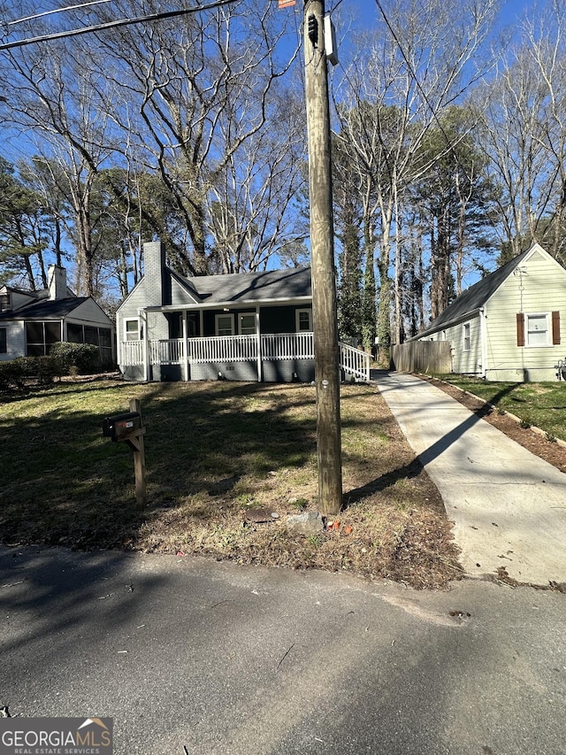 view of front facade featuring a porch, a front yard, concrete driveway, and a chimney