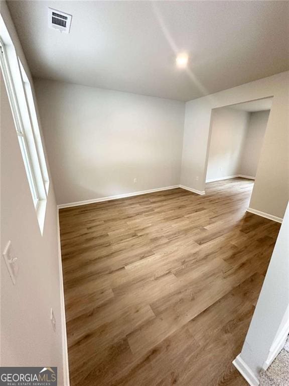 empty room with wood finished floors, visible vents, and baseboards