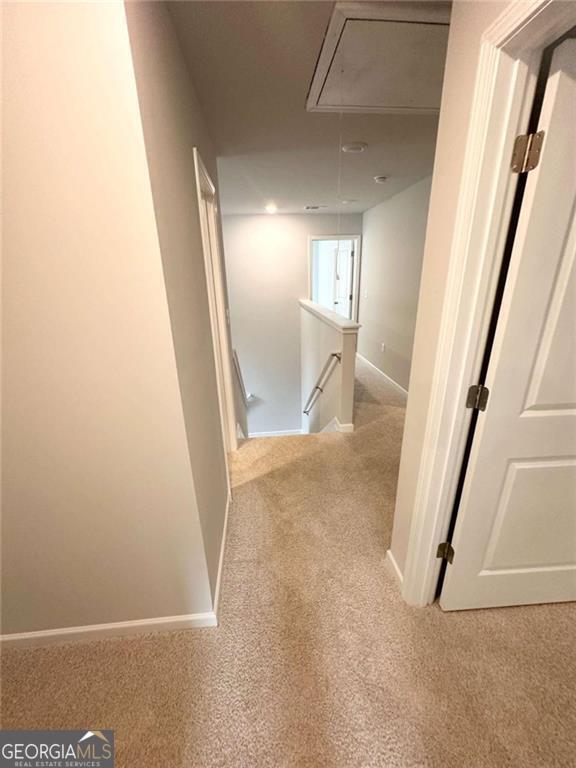 hallway featuring attic access, baseboards, carpet flooring, and an upstairs landing