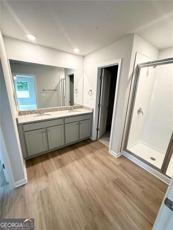 full bath featuring double vanity, a shower stall, a sink, and wood finished floors