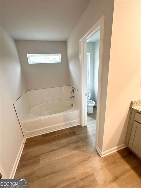 full bath featuring toilet, wood finished floors, vanity, baseboards, and a bath