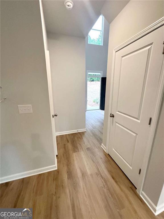 corridor featuring light wood-style flooring, baseboards, and vaulted ceiling