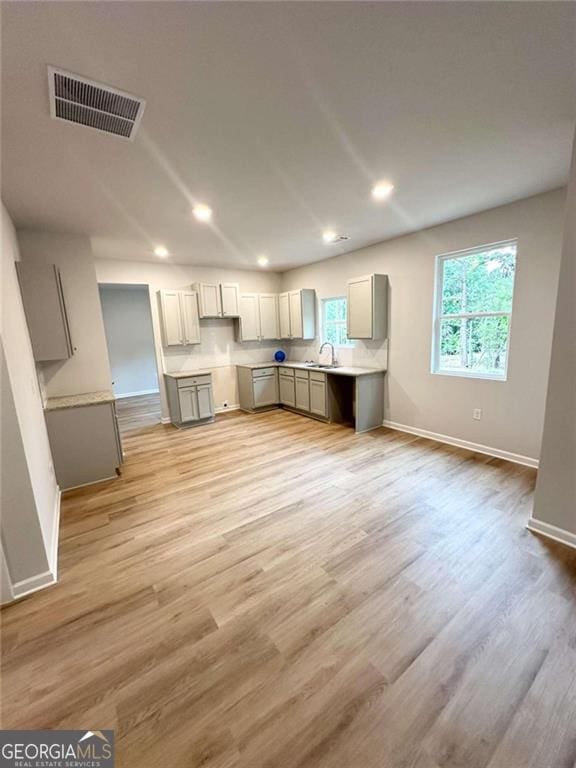 kitchen with light wood-type flooring, gray cabinets, visible vents, and a sink