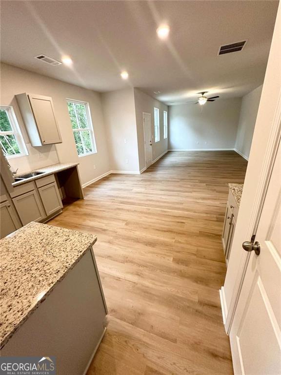 kitchen with light stone counters, light wood finished floors, visible vents, open floor plan, and baseboards