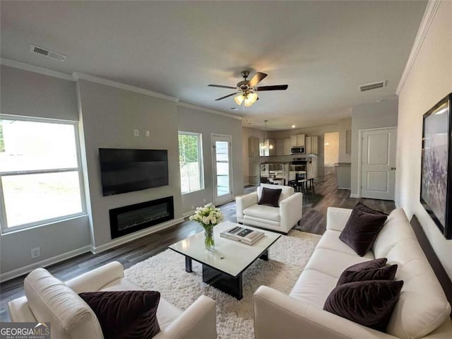 living area with crown molding, visible vents, a glass covered fireplace, wood finished floors, and baseboards