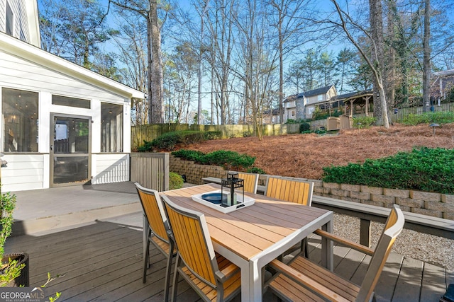 wooden terrace featuring outdoor dining space, fence, and a sunroom