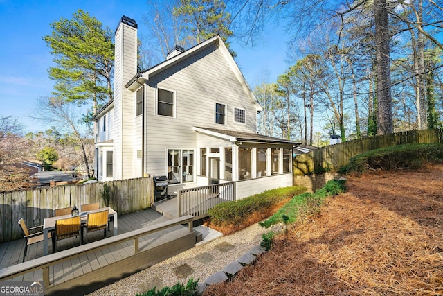 rear view of house with a deck, outdoor dining area, fence, a sunroom, and a chimney