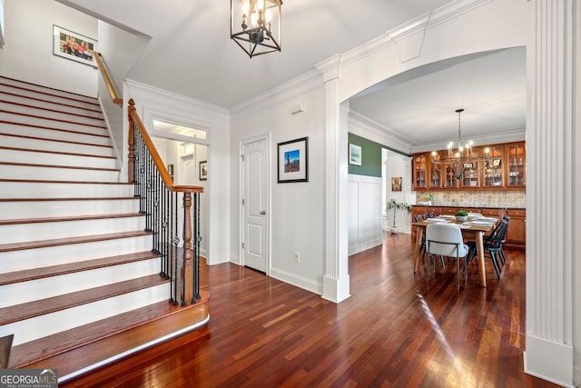 entryway featuring arched walkways, a notable chandelier, stairs, ornamental molding, and dark wood-style floors