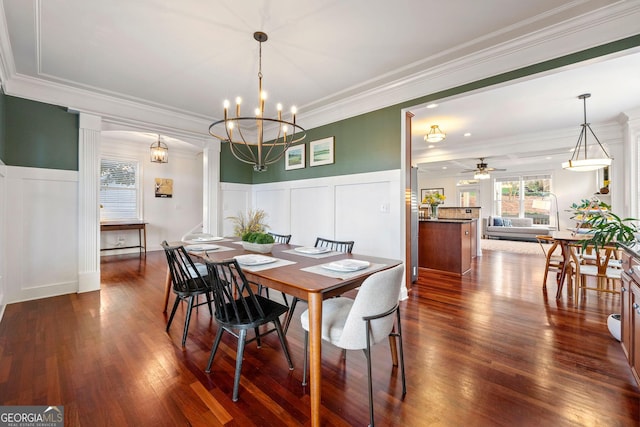 dining room with a decorative wall, a wainscoted wall, ceiling fan with notable chandelier, dark wood-style flooring, and ornamental molding