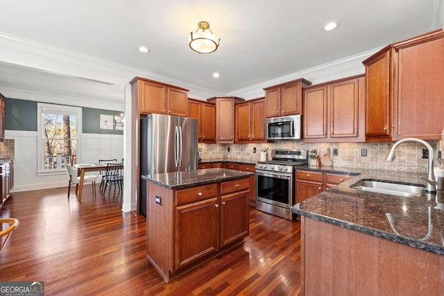 kitchen with a sink, dark wood-style floors, appliances with stainless steel finishes, brown cabinets, and dark stone counters