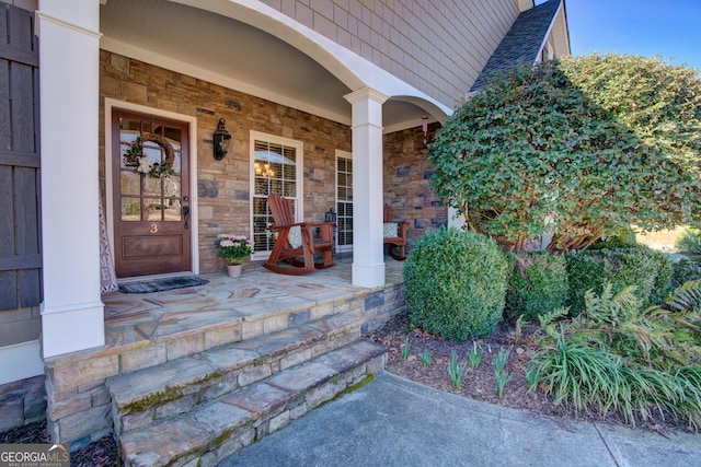 property entrance with a porch, stone siding, and roof with shingles