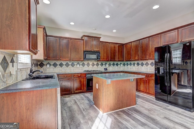 kitchen featuring tasteful backsplash, light wood-style flooring, a center island, black appliances, and a sink