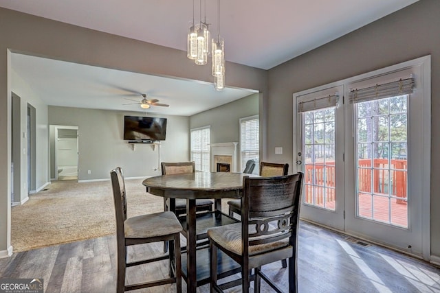 dining room featuring a fireplace, visible vents, ceiling fan, wood finished floors, and baseboards