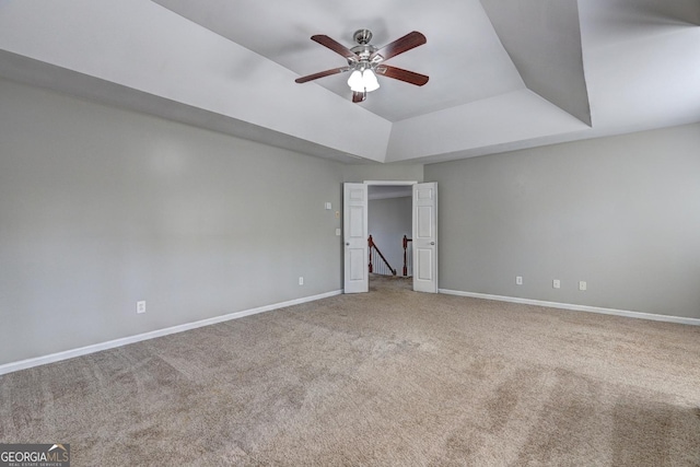 carpeted empty room featuring a ceiling fan, a raised ceiling, and baseboards