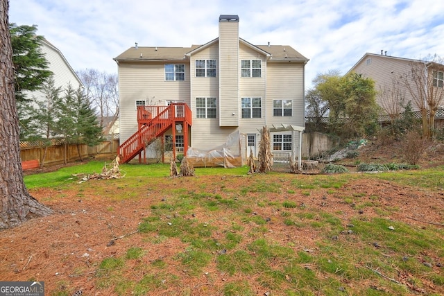 back of house featuring fence, stairs, a lawn, a wooden deck, and a chimney