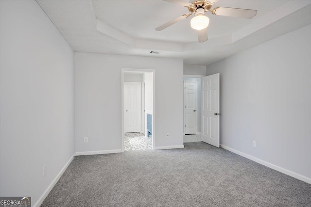 unfurnished bedroom with ceiling fan, carpet flooring, visible vents, baseboards, and a raised ceiling