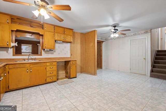 kitchen featuring wallpapered walls, brown cabinetry, a ceiling fan, light countertops, and a sink