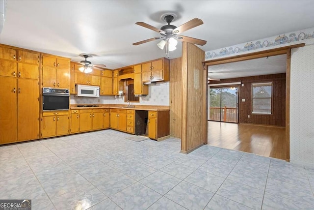 kitchen featuring white microwave, brown cabinetry, wallpapered walls, and black oven