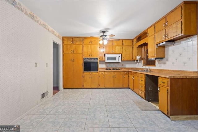 kitchen featuring visible vents, brown cabinetry, a sink, black appliances, and wallpapered walls