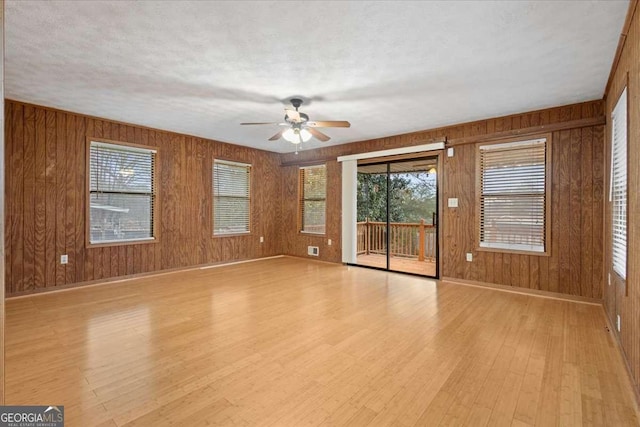 unfurnished living room featuring light wood finished floors, ceiling fan, wooden walls, a textured ceiling, and baseboards