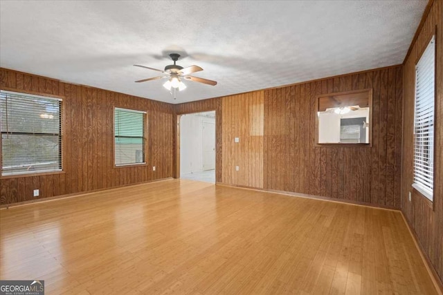 spare room with light wood-style floors, wood walls, a textured ceiling, and a ceiling fan