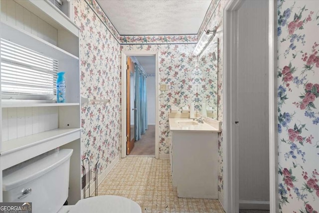 bathroom with wallpapered walls, toilet, a textured ceiling, vanity, and tile patterned floors