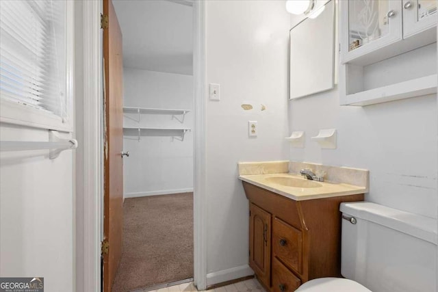 half bath featuring baseboards, vanity, and toilet