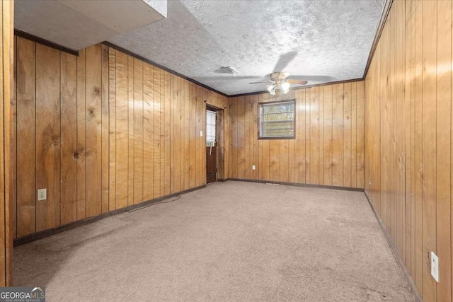 carpeted spare room featuring baseboards, ceiling fan, ornamental molding, a textured ceiling, and wood walls