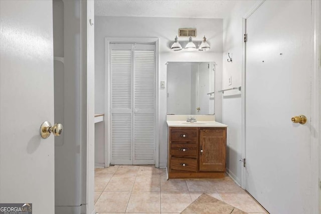 bathroom with a textured ceiling, tile patterned flooring, vanity, visible vents, and a closet