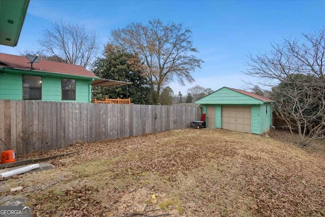 view of yard with driveway, a detached garage, fence, and an outdoor structure