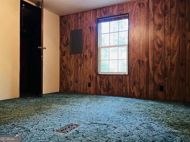 unfurnished room featuring carpet, visible vents, electric panel, and wooden walls