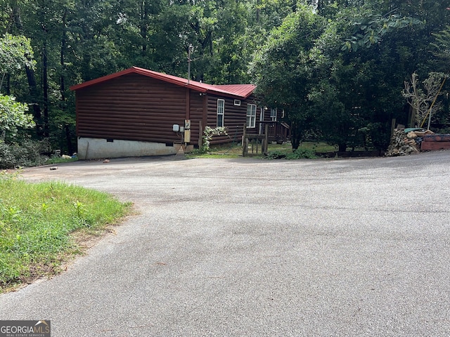 view of side of home with a forest view, crawl space, log veneer siding, and driveway