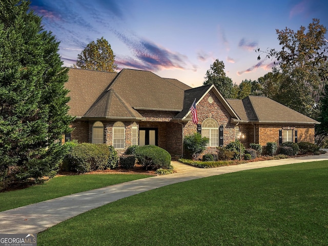 view of front of property with brick siding, roof with shingles, and a front yard