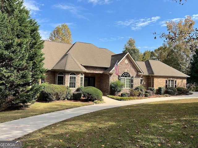 view of front of house with stone siding, a front lawn, roof with shingles, and brick siding