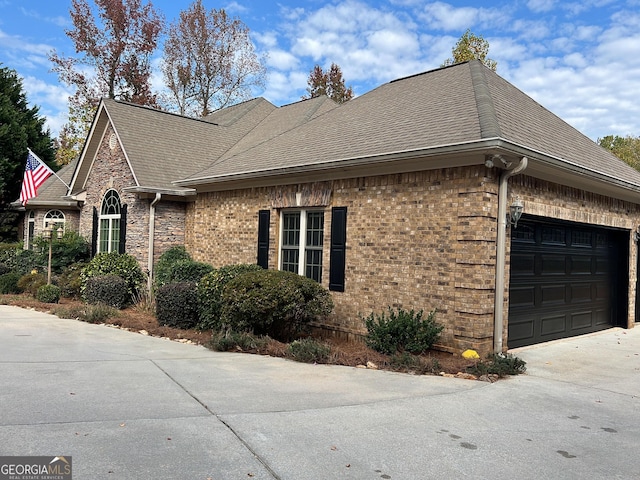 view of home's exterior featuring an attached garage, roof with shingles, concrete driveway, and brick siding