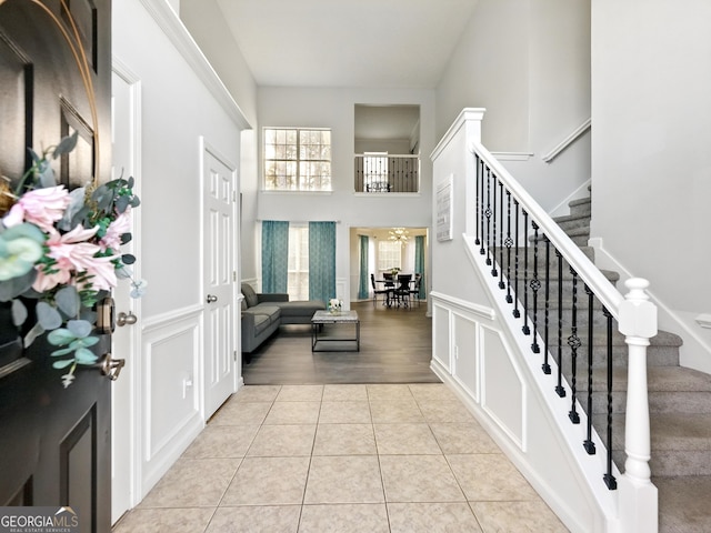 foyer entrance with light tile patterned floors, stairway, a high ceiling, and a decorative wall