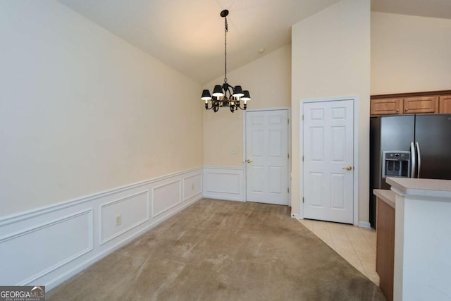 unfurnished dining area with a notable chandelier, light colored carpet, light tile patterned flooring, vaulted ceiling, and wainscoting