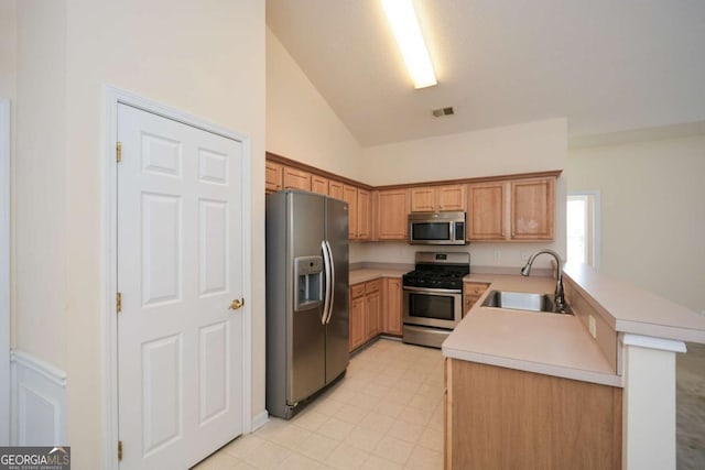 kitchen featuring lofted ceiling, light countertops, appliances with stainless steel finishes, a sink, and a peninsula