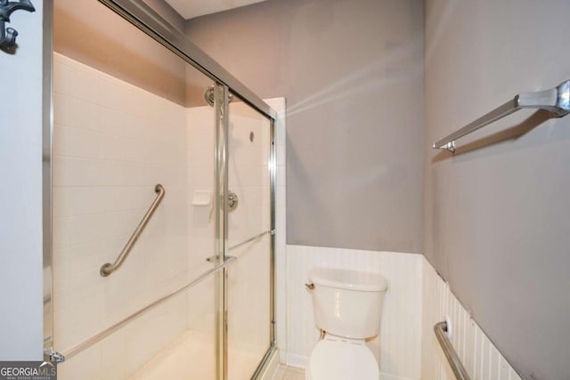 bathroom with a wainscoted wall, a stall shower, and toilet