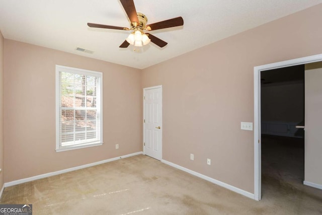 spare room with light carpet, ceiling fan, visible vents, and baseboards