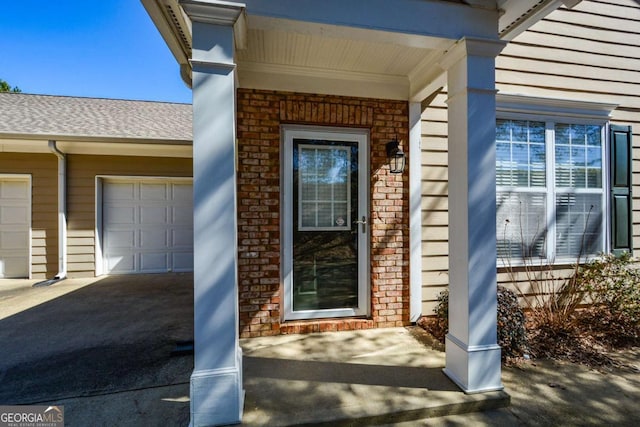 entrance to property featuring a shingled roof, brick siding, and an attached garage