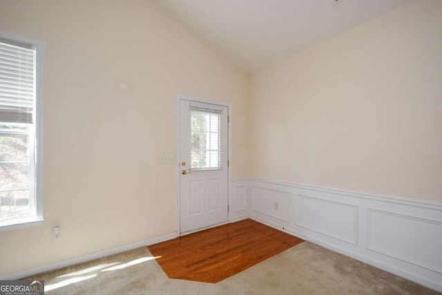 doorway to outside with lofted ceiling, a decorative wall, carpet flooring, and wainscoting