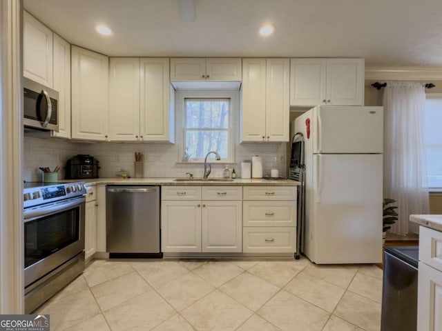 kitchen with light stone countertops, a sink, white cabinetry, appliances with stainless steel finishes, and decorative backsplash