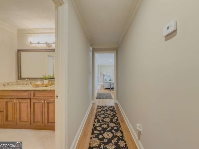 hallway with a sink, light wood-style flooring, baseboards, and crown molding